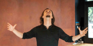 Male student with long brown hair and beard leaning back and opening arms in expressive arts dance moment