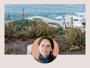 Daria Halprin portrait, mature woman with dark brown hair smiling, with plants and ocean in background.