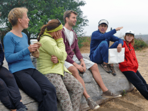 Ken Otter, middle-aged white male, sitting on log at beach with 4 adult students, white men and women