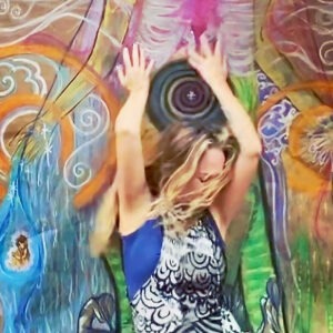 blonde woman with long hair wearing black and white top reaching upwards against a brightly colored self-portrait drawing