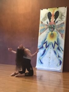 woman with long brown hair back bending on her knees in front of her life-sized self portrait drawing in the Halprin Life/Art Process