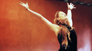 woman with long red hair reaching arms out above her head with and expression of joy