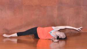 White woman in 30s lying down on her side with arm outstretched above her and leg below in a spiral