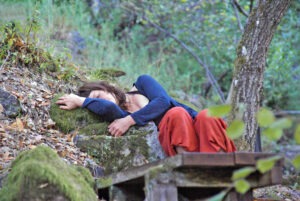 Woman contouring to stones lying on her side wearing blue shirt and orange pants closing eyes in peaceful repose